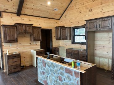 Rustic kitchen under construction with stone island and wooden cabinets.