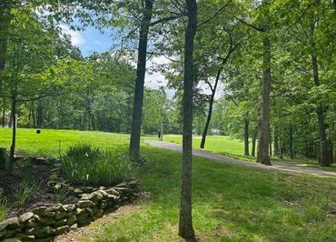 A peaceful park scene with trees, grass, and a stone-lined flower bed.
