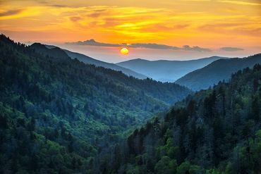 Sunset over lush forested mountains with vibrant sky.