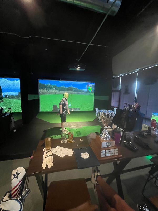 Person playing indoor golf simulator with trophy on table.
