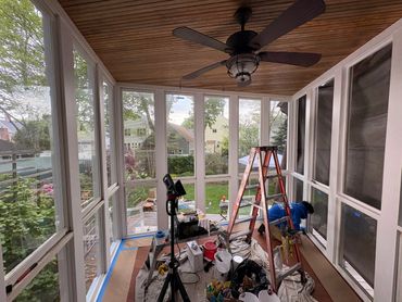 Worker renovating a sunroom with tools and ladder inside.