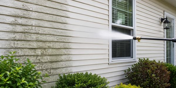 Pressure washing a dirty house exterior to clean mold and grime.