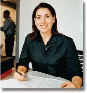 Smiling woman in a black shirt working at a desk with papers and a pen.