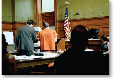 A courtroom scene with a defendant in an orange jail uniform and a lawyer.