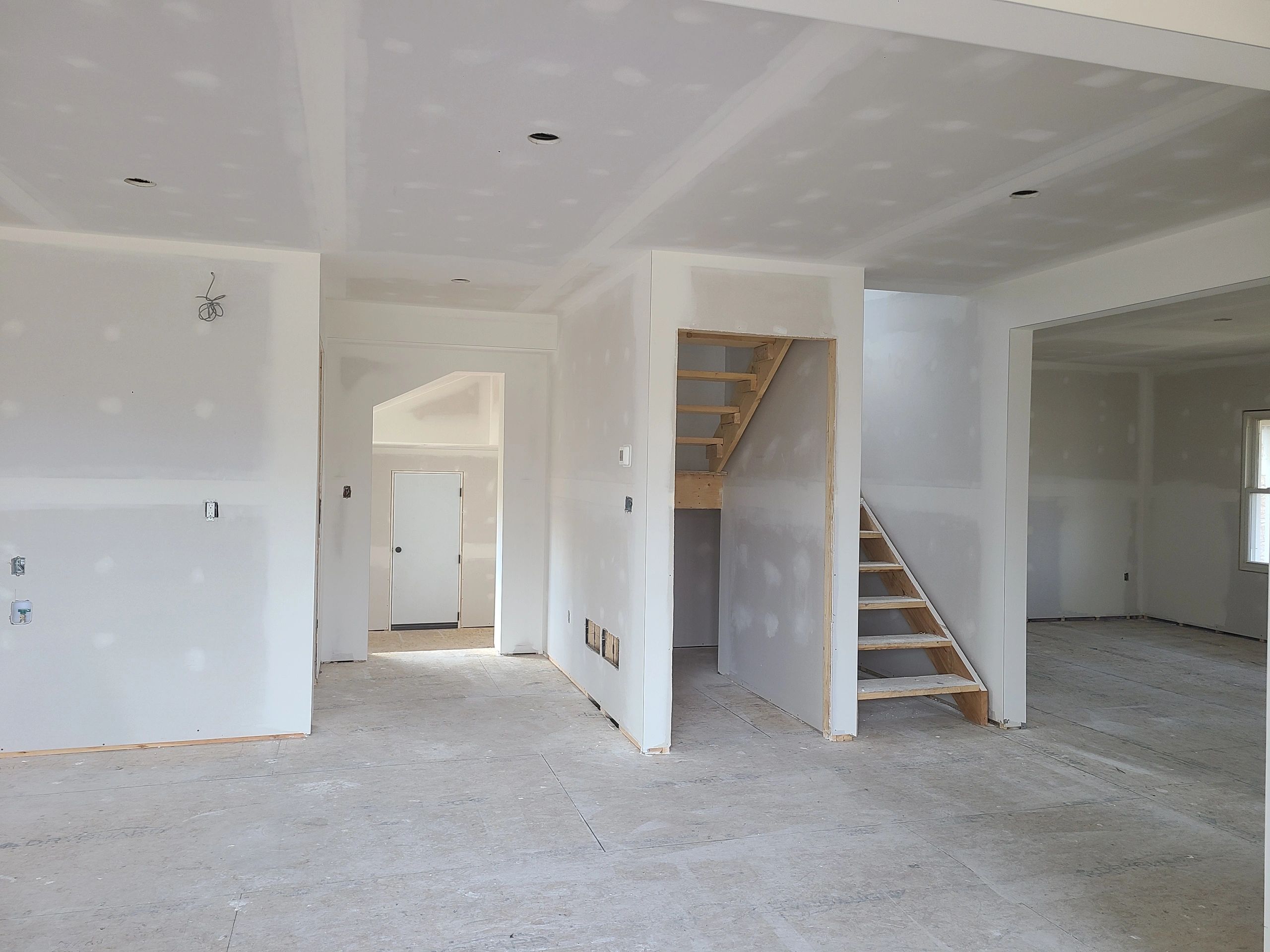 Interior of a house under construction with drywall and unfinished stairs.