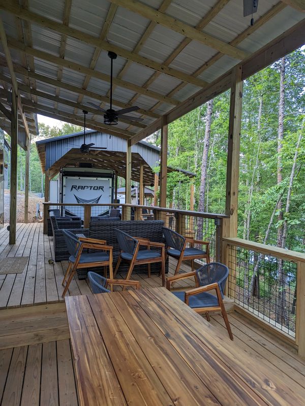 Covered wooden deck with outdoor seating and ceiling fans overlooking green trees.