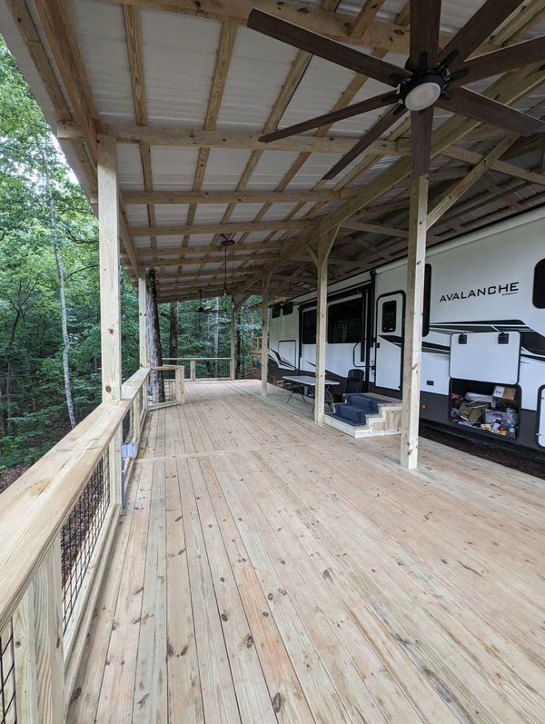 Spacious wooden deck with ceiling fans next to an Avalanche RV in a forest setting.