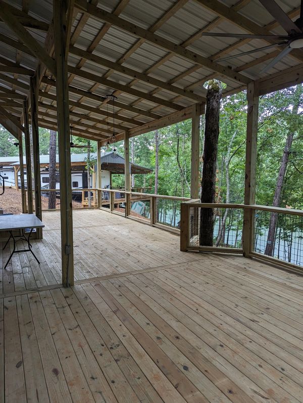 Spacious wooden deck with roof and tree integration, overlooking a wooded area.