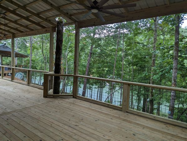 Spacious wooden deck overlooking a lush forest and lake.