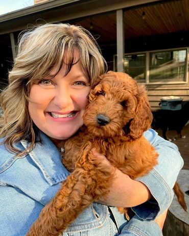 Woman joyfully holding a fluffy brown puppy outdoors.