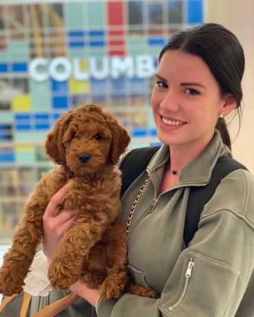 A woman smiling while holding a fluffy brown puppy indoors.