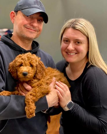 Couple smiling and holding a fluffy brown puppy indoors.