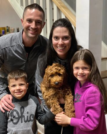 Happy family posing with their curly-haired brown dog indoors.