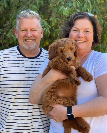 Happy couple smiling with their adorable fluffy brown puppy outdoors.