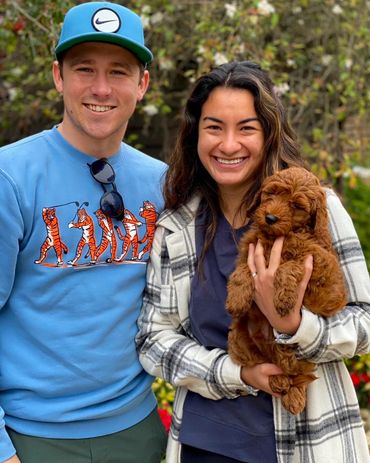 Happy couple smiling outdoors while holding an adorable brown puppy.