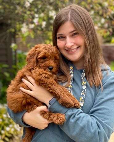 Young woman smiling while holding a fluffy brown puppy outdoors.