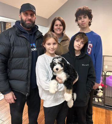 Family of five with a black and white puppy indoors.