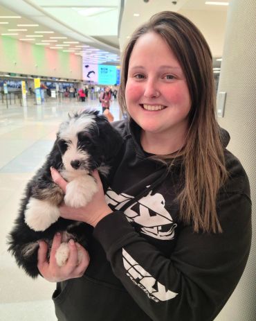 Smiling woman holding a fluffy black and white puppy indoors.