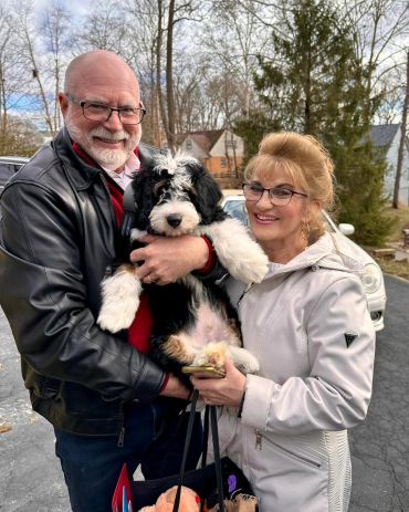 A happy couple holding a fluffy black and white puppy outdoors.