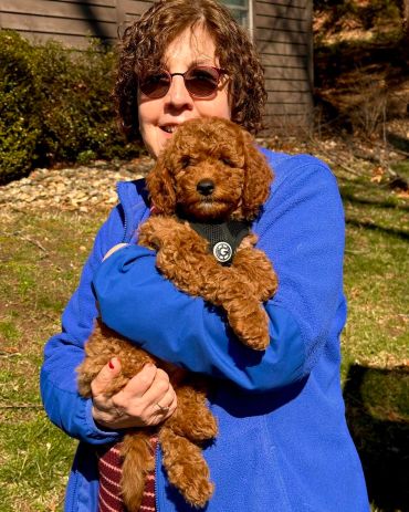 Woman in blue jacket holding a curly-haired brown puppy outdoors.