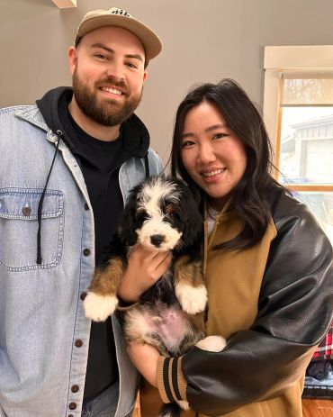 Smiling couple holding an adorable fluffy puppy together indoors.