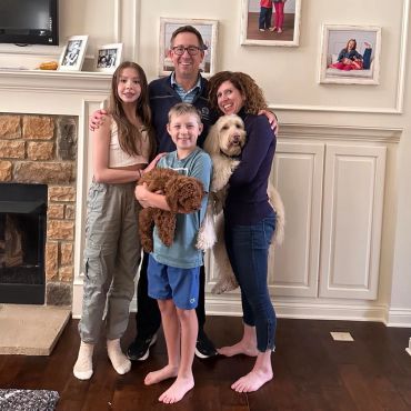 A happy family of four with two dogs posing in their living room.