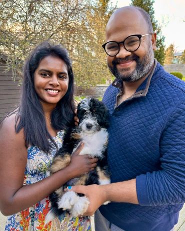 A happy couple holding a fluffy black and white puppy outdoors.