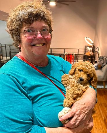 Smiling woman in turquoise holding a curly-haired puppy indoors.