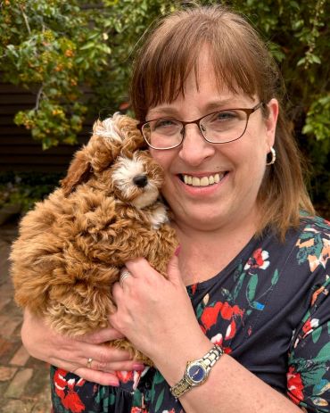 Woman joyfully holding a fluffy brown and white puppy outdoors.