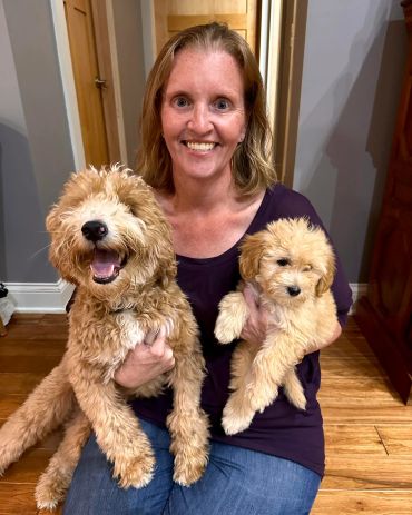 Woman smiling while holding two fluffy dogs indoors.