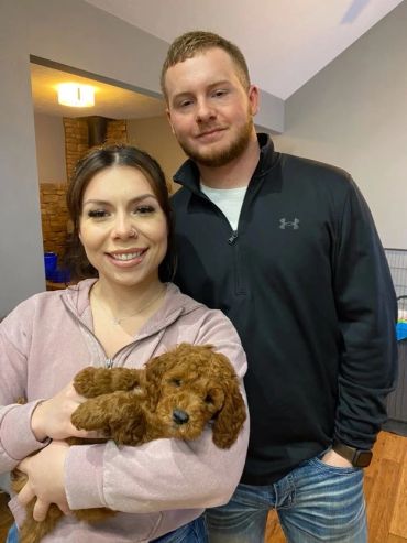 A smiling couple holding a small brown puppy indoors.