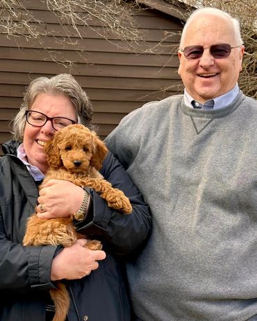 Happy couple holding an adorable curly-haired puppy outside.
