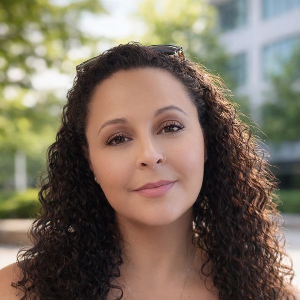 Close-up portrait of a woman with curly hair and a nose ring outdoors.