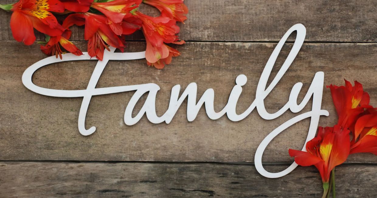 The word "Family" in white cursive on wood with red flowers.