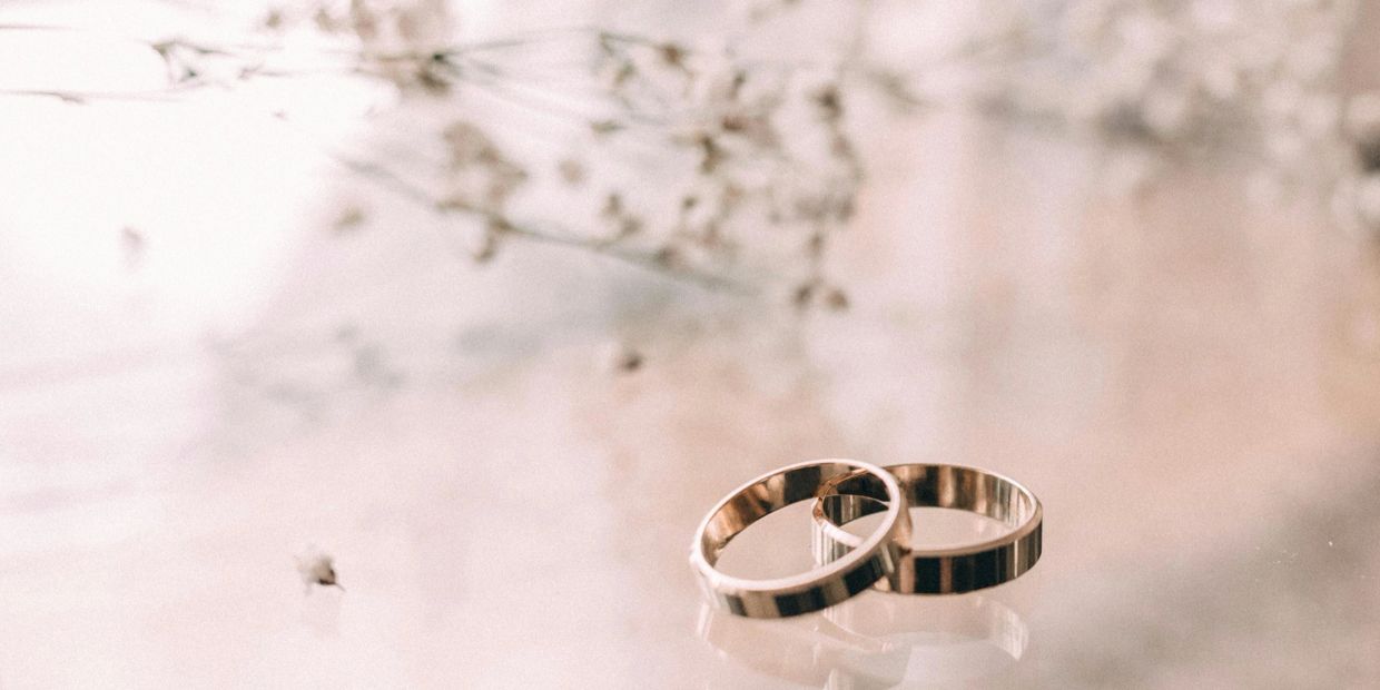 Two gold wedding rings on a soft, reflective surface with delicate floral background.