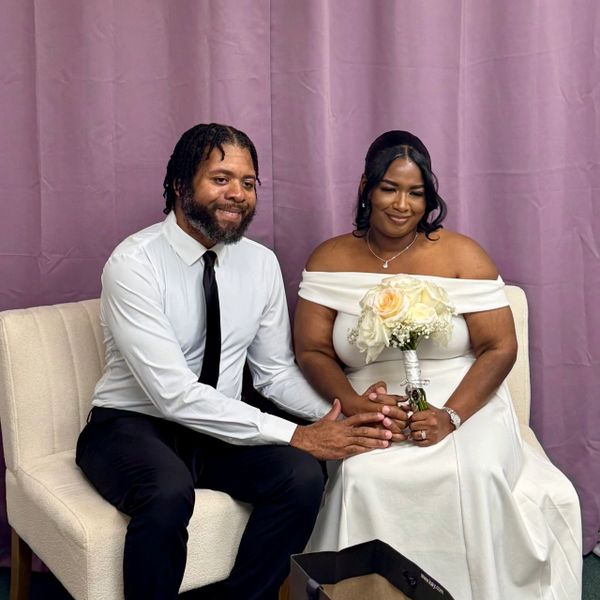A couple dressed elegantly, sharing a tender moment with a bouquet.