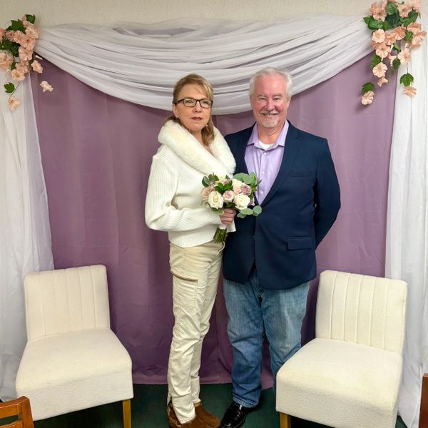 Couple posing indoors with flowers and decorative backdrop.