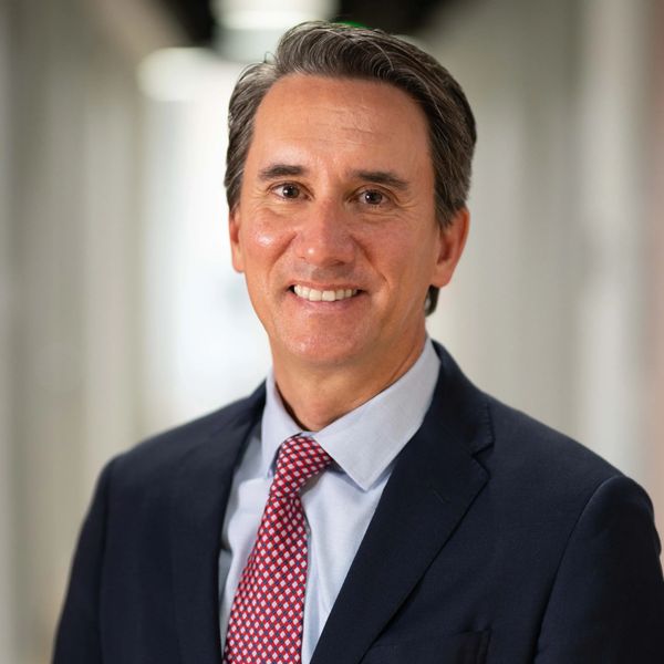 A smiling man in a suit and red patterned tie.
