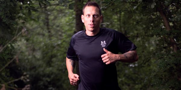 Man jogging in a forest wearing a black sports shirt.