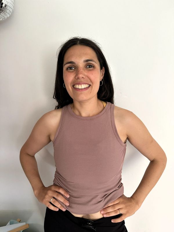 Smiling woman in a mauve sleeveless top standing with hands on hips.