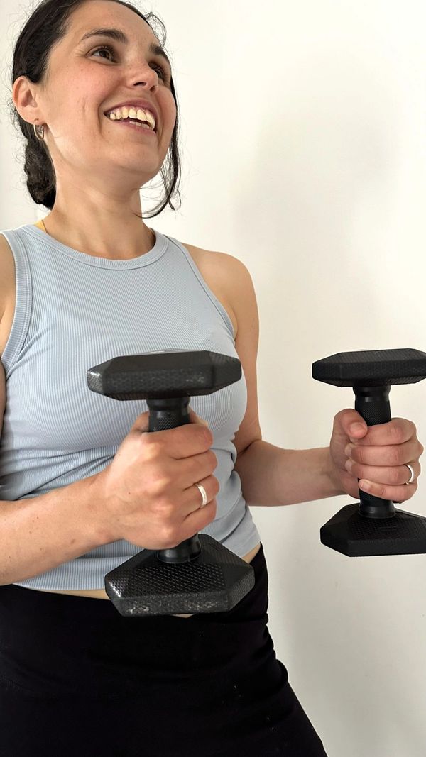 Smiling woman lifting black dumbbells in a workout.