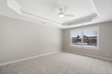 Empty bedroom with beige carpet, tray ceiling, and large window.
