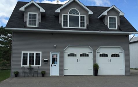 A gray two-story garage with white doors and windows under a partly cloudy sky.