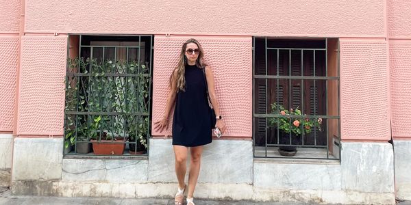 Woman in black dress standing against a pink wall with windows.