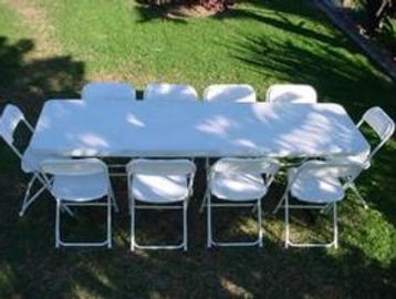 White folding table and chairs set outdoors on grass.