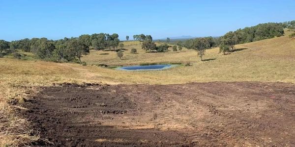 Freshly plowed field with a small pond and rolling hills in the background.