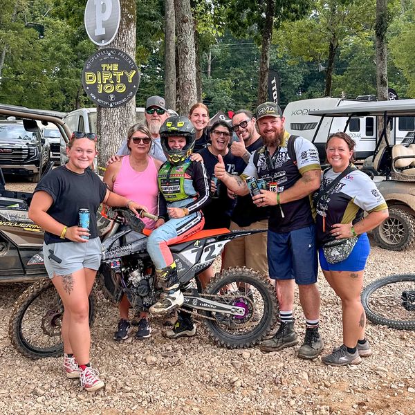 Group celebrating with motocross rider by a bike at The Dirty 100 event.