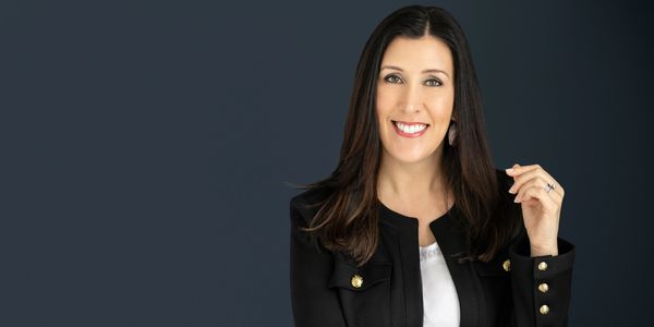 Smiling woman in a black blazer with long dark hair.