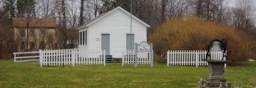 Small white community building with picket fence and sign in front.