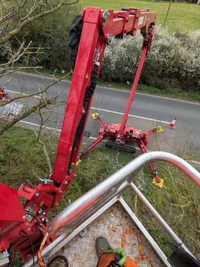 Aerial view of a red cherry picker lifting a worker above a road and trees.